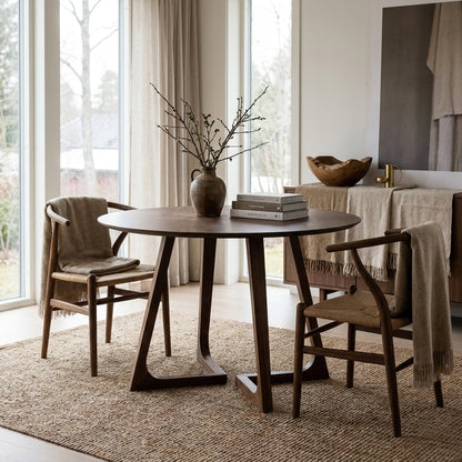 Minimalist dining room with a round wooden table, woven chairs, and neutral decor in a bright, modern Scandinavian home.